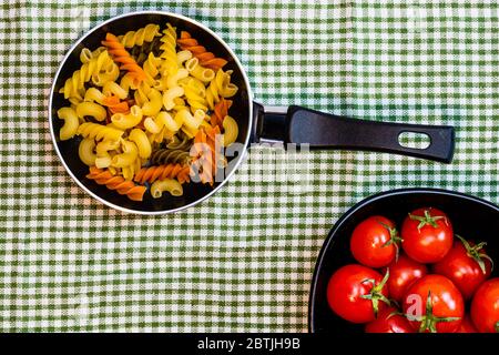 Small mini frying pan with tricolor raw fusilli pasta in a rustic composition. Stock Photo