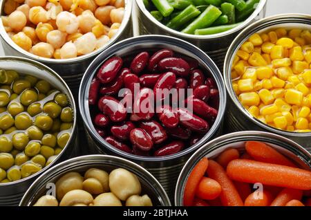 Canned vegetables in opened tin cans on kitchen table. Non-perishable long shelf life foods background Stock Photo