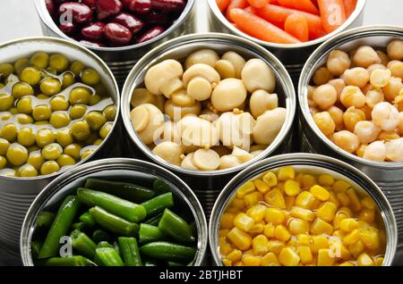 Canned vegetables in opened tin cans on kitchen table. Non-perishable long shelf life foods background Stock Photo