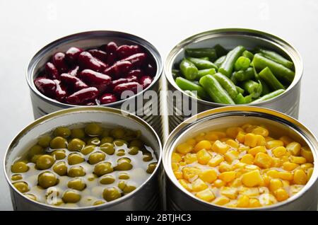 Canned kidney beans, green beans, peas and corn in opened tin cans on kitchen table. Non-perishable foods background Stock Photo