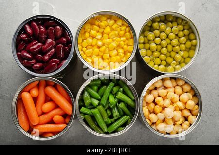 Flat lay view at canned carrots, chickpeas, kidney beans, green beans, peas and corn in opened tin cans on kitchen table. Non-perishable foods backgro Stock Photo