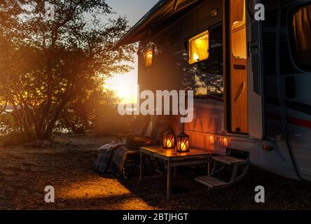 Road Trip Adventures. Calm Warm Night on a Camping. Camper Van, Outdoor Chairs and Romantic Light From Lanterns. Vacation in Recreational Vehicle. Stock Photo