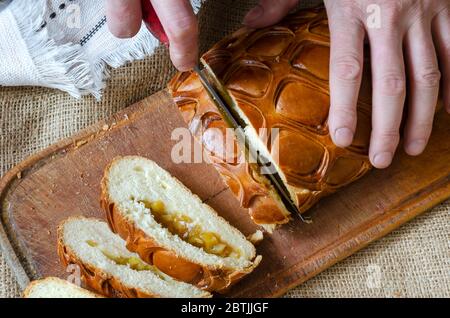 A man slices into pieces a traditional homemade apple pie. Hands of an adult male serving a sweet pie in portions on a cutting board. View from above. Stock Photo