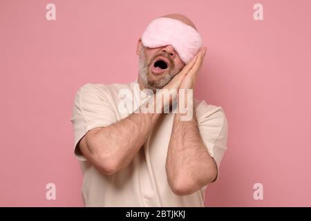 Mature man in sleeping mask yawning while waking up. Stock Photo
