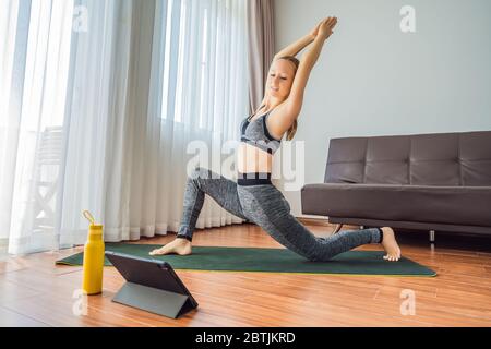 Fitness woman exercising on the floor at home and watching fitness videos in a tablet. People do sports online because of the coronovirus Stock Photo