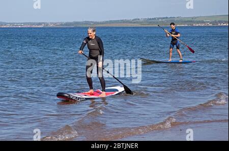 Portobello, Edinburgh, Scotland, UK. 26 May 2020. More relaxed atmosphere at the seaside late afternoon as Scotland nears the end of Phase 1 of Coronavirus Lockdown. Temperature of 19 degrees and sunny. Pictured the Harrison family, mum and her sons enjoy stand up paddle boarding. Stock Photo