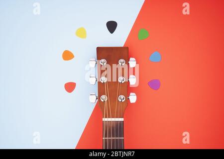 Colorful picks around acoustic guitars headstock. Flat lay on light blue and red background Stock Photo