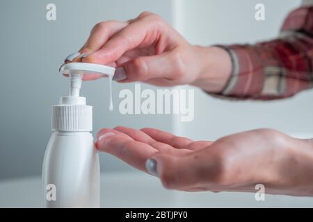 Woman pushing dispenser, squeezing out antiseptic gel on palm, cleaning hands - close up side view. Disinfection, protection, prevention, COVID-19 Stock Photo