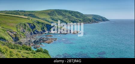 A colourful wide panoramic taking in the rural coastline of South East Cornwall from Lantivet Bay through to Polperro on a beautiful late Spring day. Stock Photo