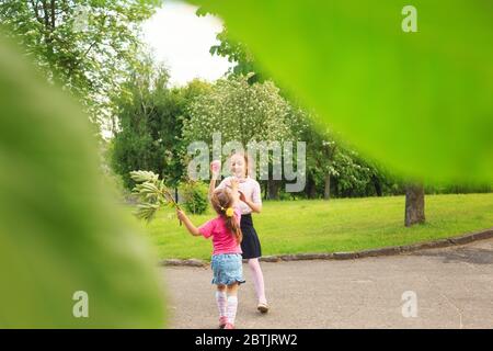 Two happy cute little sisters jumping with colorful toy balloon outdoors. Smiling kids having fun in green spring garden at summer day. Stock Photo