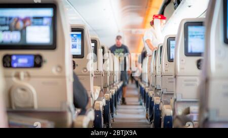 Interior of large passengers airplane with people on seats and stewardess in uniform walking the aisle. Stock Photo