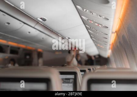 Interior of large passengers airplane with people on seats and stewardess in uniform walking the aisle. Stock Photo