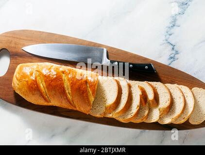 sliced loaf of bread on a cutting board and a chef's knife on a marble table Stock Photo