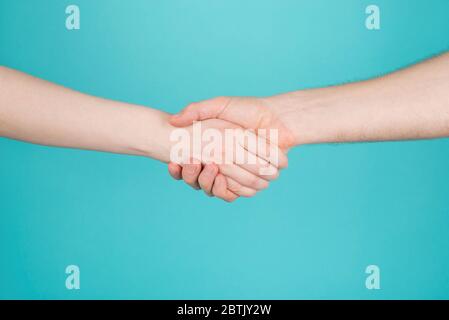 Close-up cropped photo of two persons woman and man holding hands as greeting isolated on turquoise teal blue color bright background Stock Photo