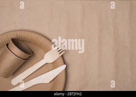 Top above overhead view photo of wooden cutlery and paper cups and plate placed in the left bottom corner isolated on craft paper background table Stock Photo