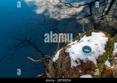 The compass is lying on the snow on the lake shore . The arrow points to the North Stock Photo