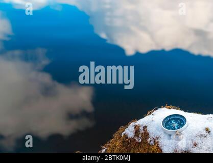 The compass is lying on the snow on the lake shore . The arrow points to the North Stock Photo