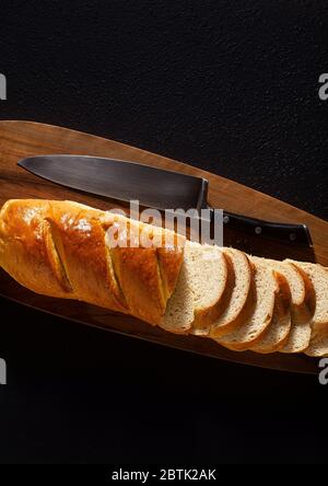 sliced loaf of bread on a chopping board and a chef's knife on a black background Stock Photo