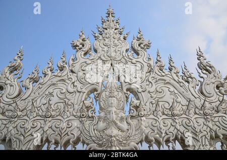 An amazing sculpture with a buddha image and dragons dominates the bridge to Wat Rong Khun, the beautiful white temple in Chiang Rai Stock Photo