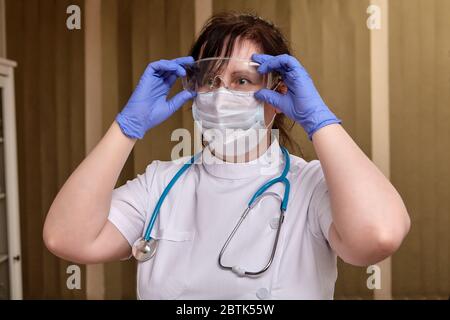 Female doctor in uniform, facial protective medical mask, safety glasses, gloves and with stethoscope is going to help patients during coronavirus cov Stock Photo