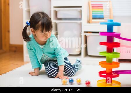 toddler girl play marble run game at home against white background Stock Photo