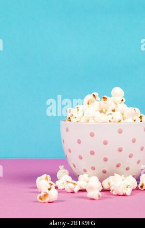Fresh popcorn in a white pink bowl on pink and blue background Stock Photo
