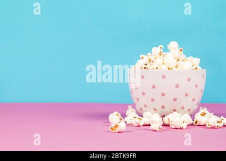 Fresh popcorn in a white pink bowl on pink and blue background Stock Photo