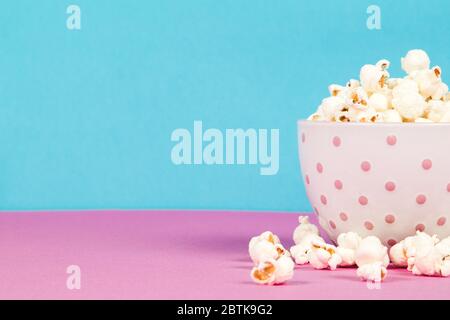 Fresh popcorn in a white pink bowl on pink and blue background Stock Photo