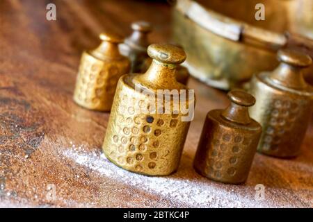 Old copper brass scale weights with calibration marks on wooden table with flour in a bakery. Image with selective focus. Stock Photo