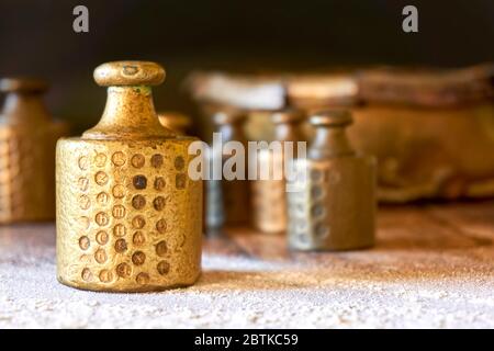 Old copper brass scale weights with calibration marks on wooden table with flour in a bakery. Image with selective focus. Stock Photo