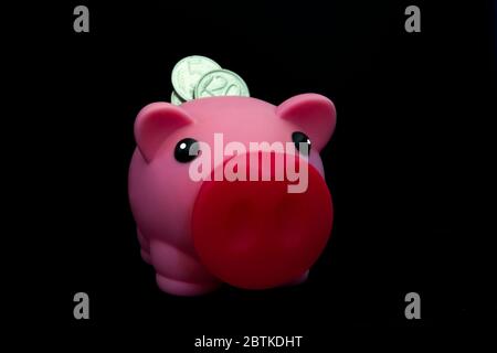 Pink piggy bank full of coins on a black background. Concept of where to invest your savings. Make money Stock Photo