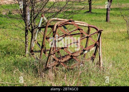 Old vintage retro rusted abandoned agricultural farming equipment used to work with tractors on soil left in uncut grass in family house orchard Stock Photo