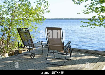 two reclining chairs wait for their owners to come and enjoy their morning coffee in front of a beautiful, relaxing view of the river. Stock Photo