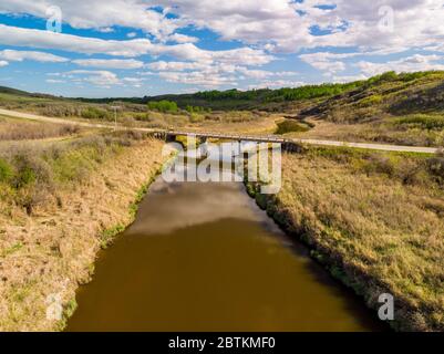 An aerial view of a old bridge over calm stream running through a valley in the prairie province of Saskatchewan Stock Photo
