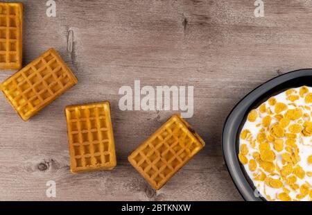 plate with cornflakes in milk and waffles on a wooden background. top view, copy space. 