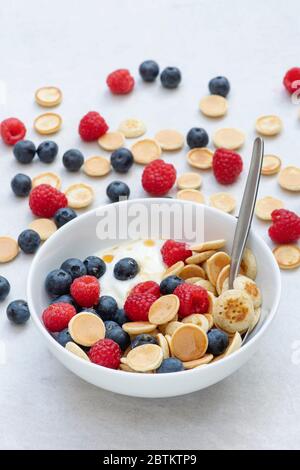 Bowl of homemade mini cereal pancakes with blueberries raspberries yogurt and maple syrup Stock Photo