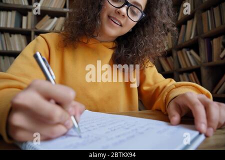 Hispanic teen girl student writing in workbook doing homework, close up. Stock Photo