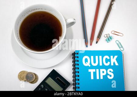 QUICK TIPS concept. Blue notebook, stationery and calculator, coffee mug on a white office table Stock Photo