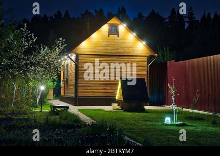 Backside of Illuminated Wooden House with Well in the Dusk Stock Photo