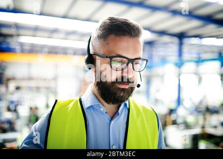Front view of technician or engineer with headset standing in industrial factory. Stock Photo