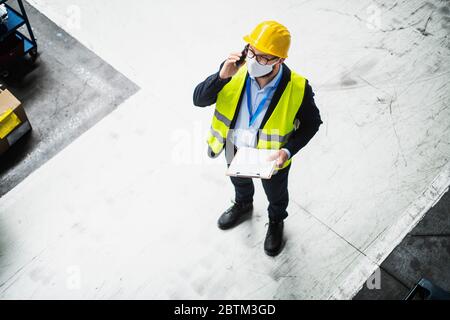 Technician or engineer with protective mask and helmet working in industrial factory. Stock Photo