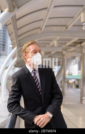 Mature businessman with mask thinking while leaning on handrail at the footbridge Stock Photo