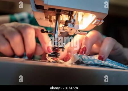 Female hands sew a protective mask using a modern electric sewing machine. Concept of safety during a viral epidemic. Stock Photo