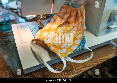Protective masks sewn of colorful material lie on a modern, electric sewing machine. Concept of safety during a viral epidemic. Stock Photo