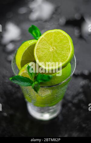 selective focus, sliced limes in a glass glass on a dark table with mint leaves Stock Photo