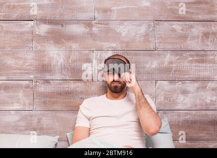 Man pulling his sleep mask before going to sleep in comfortable bed. Stock Photo