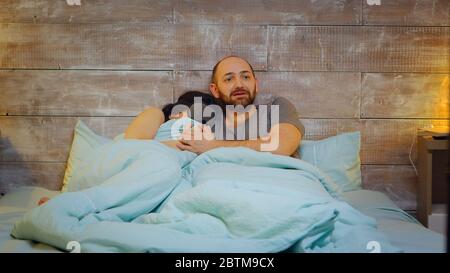 Scared young couple while watching a horror movie at tv. Couple in pajamas. Stock Photo