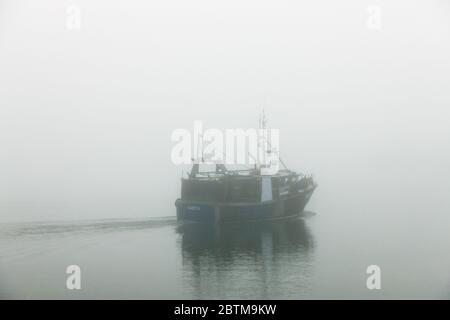 Crosshaven, Cork, Ireland. 27th May, 2020. Fishing boat Majestic IV slips away in early morning fog, as she heads for the fishing ground to check her pots for Crab in Crosshaven, Co. Cork, Ireland. Weather forcast for the day is that coastal fog will clear and become sunny everywhere with tempertures ranging between 20 to 24 degrees celcius.  - Credit; David Creedon / Alamy Live News Stock Photo