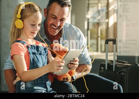 Happy father and daughter using tablet computer at airport lounge while waiting for their flight. Girl using tablet pc with her father at airport depa Stock Photo