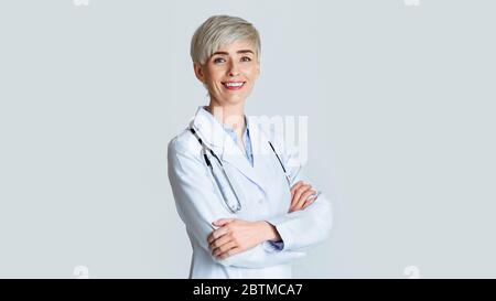 Portrait of smiling young woman doctor in white coat with stethoscope, isolated over light background Stock Photo